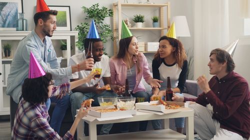 Free Group of friends enjoying a fun celebration with pizza and party hats. Stock Photo