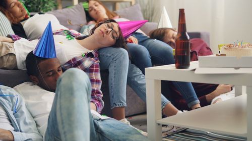 Free Young adults in party hats asleep in a living room after a celebration. Stock Photo