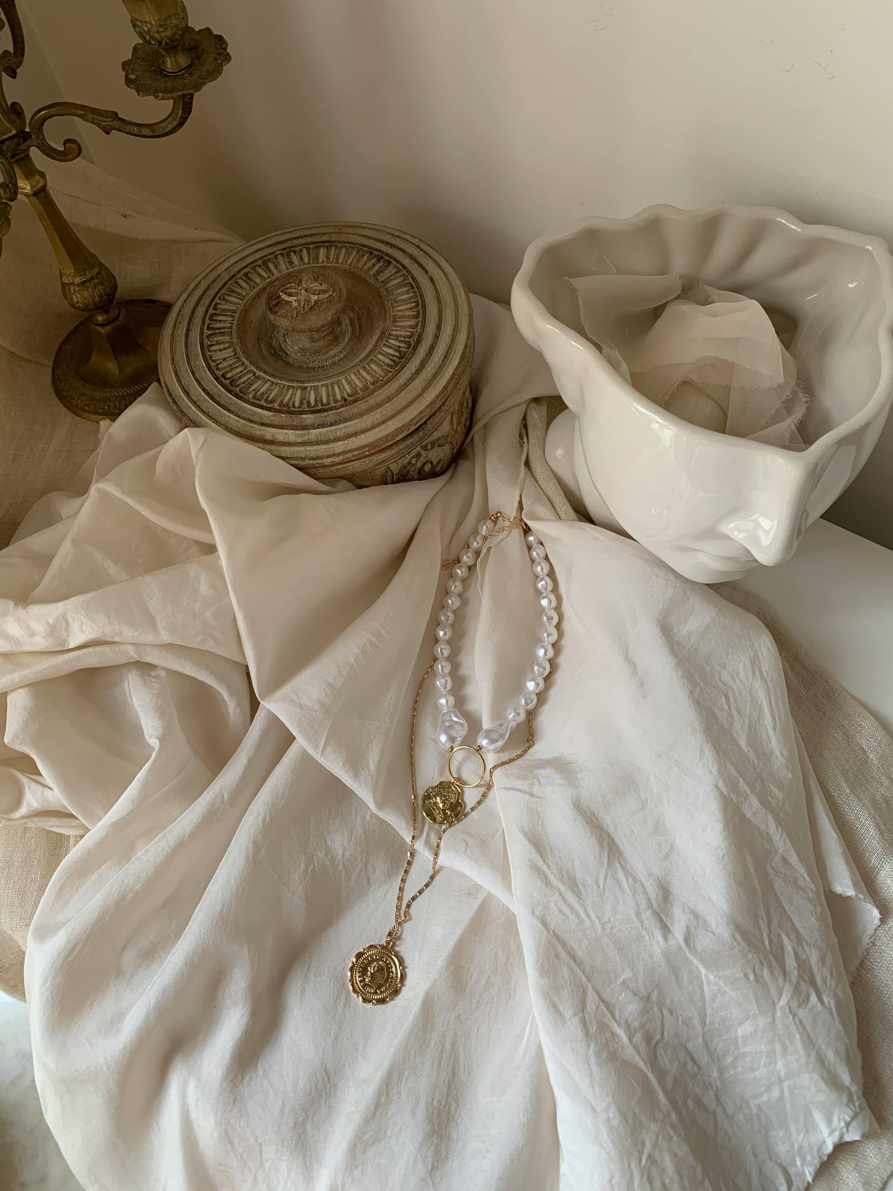 Chic arrangement of gold and pearl jewelry on a fabric, showcasing rustic and vintage decor elements.