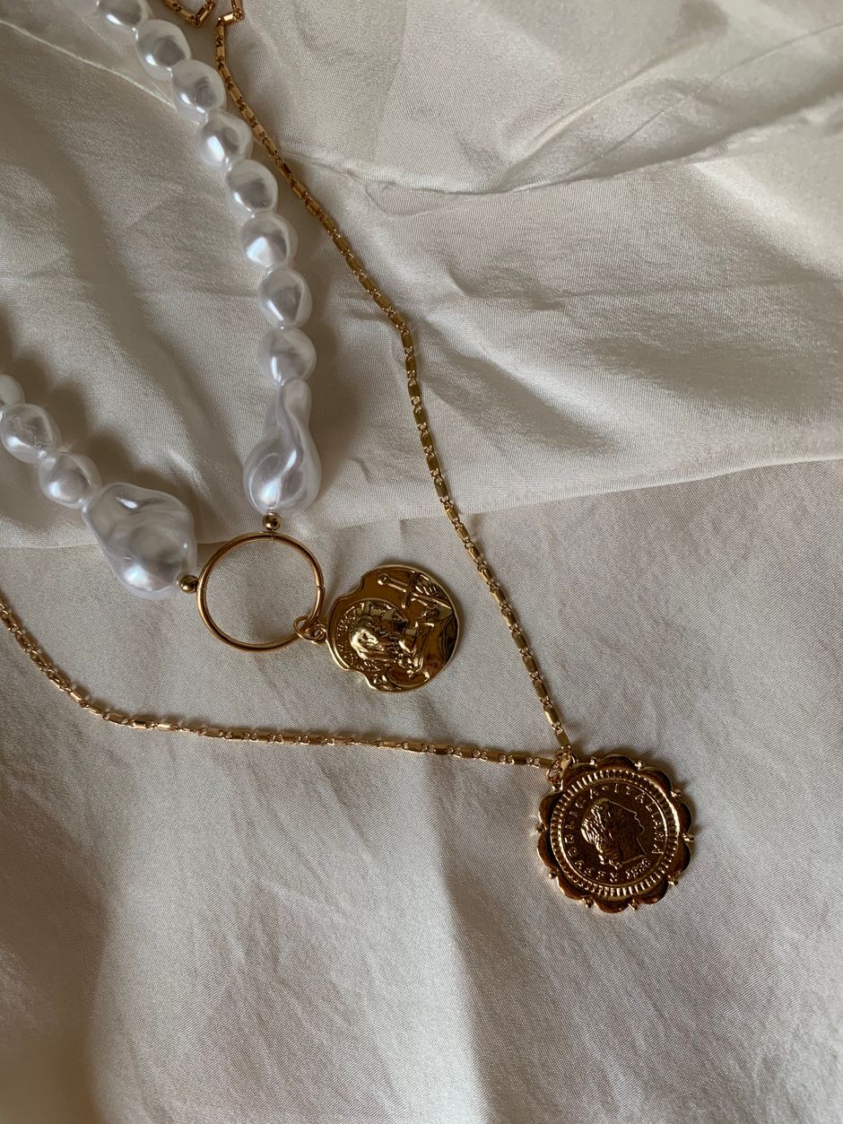 Gold medallion necklaces and a pearl strand on ivory fabric
