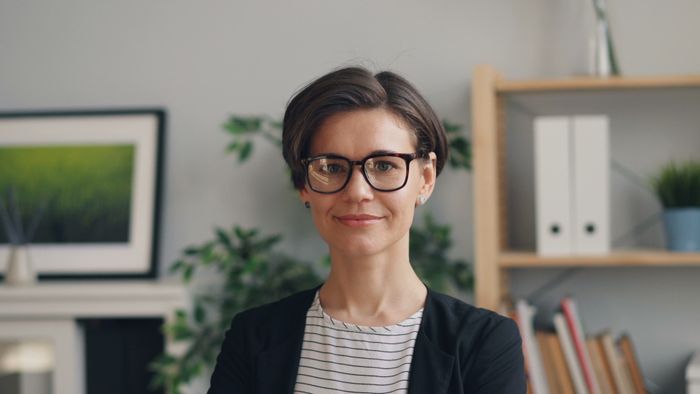 A woman with glasses standing in front of a desk