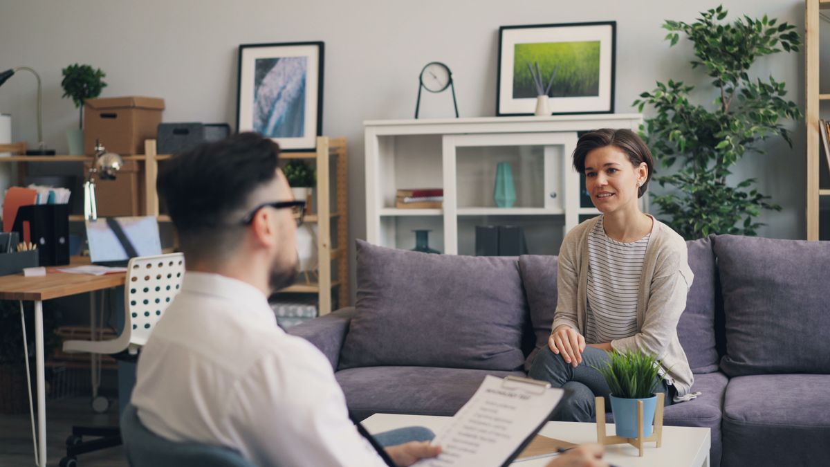 A practitioner and a client sitting together in a warm, plainly furnished consultation room, in conversation.