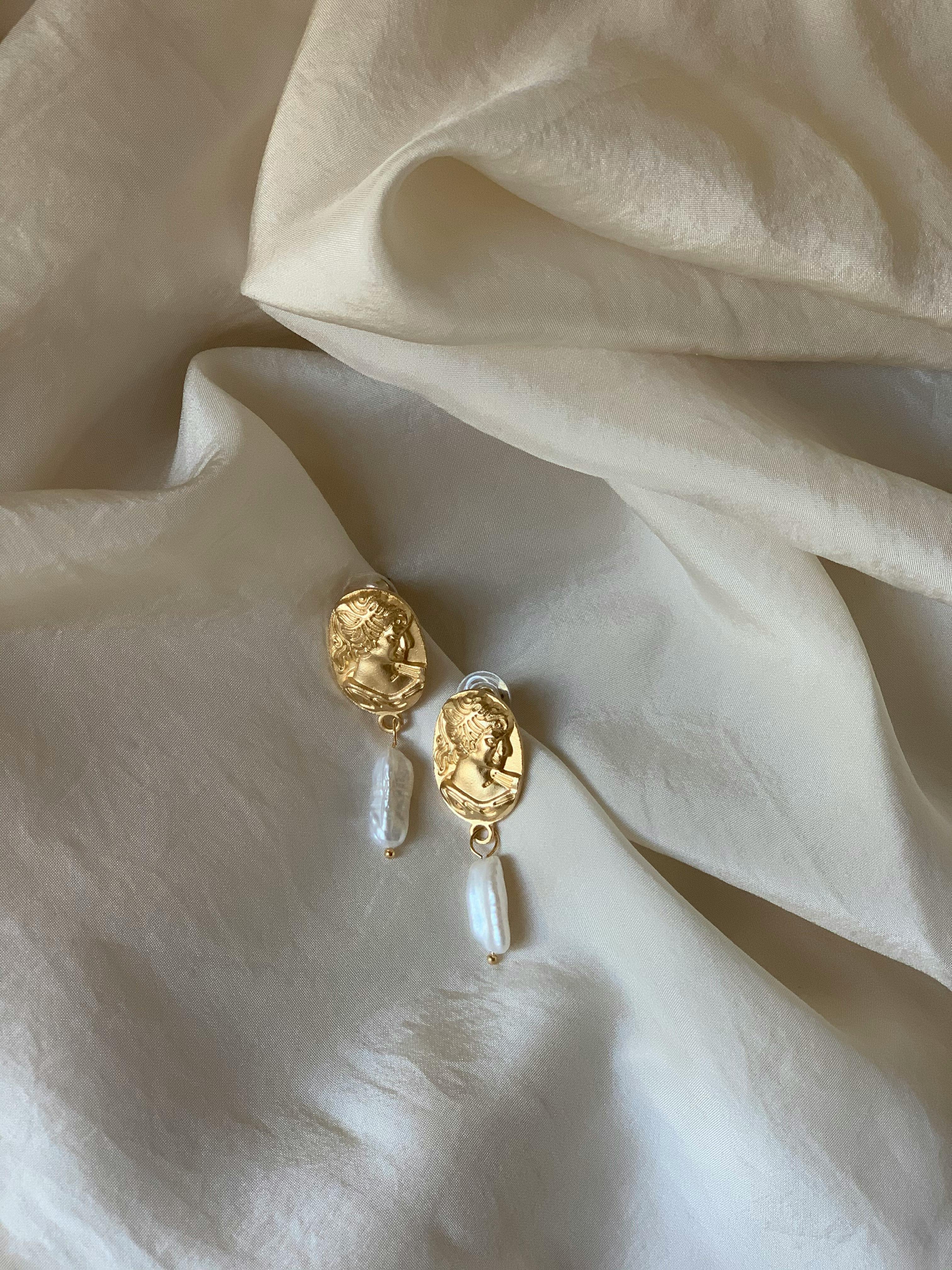 Gold earrings with pearls elegantly displayed on cream fabric for a classic look.