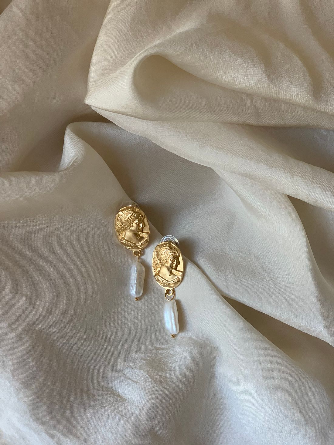 Gold earrings with pearls resting on soft cream fabric