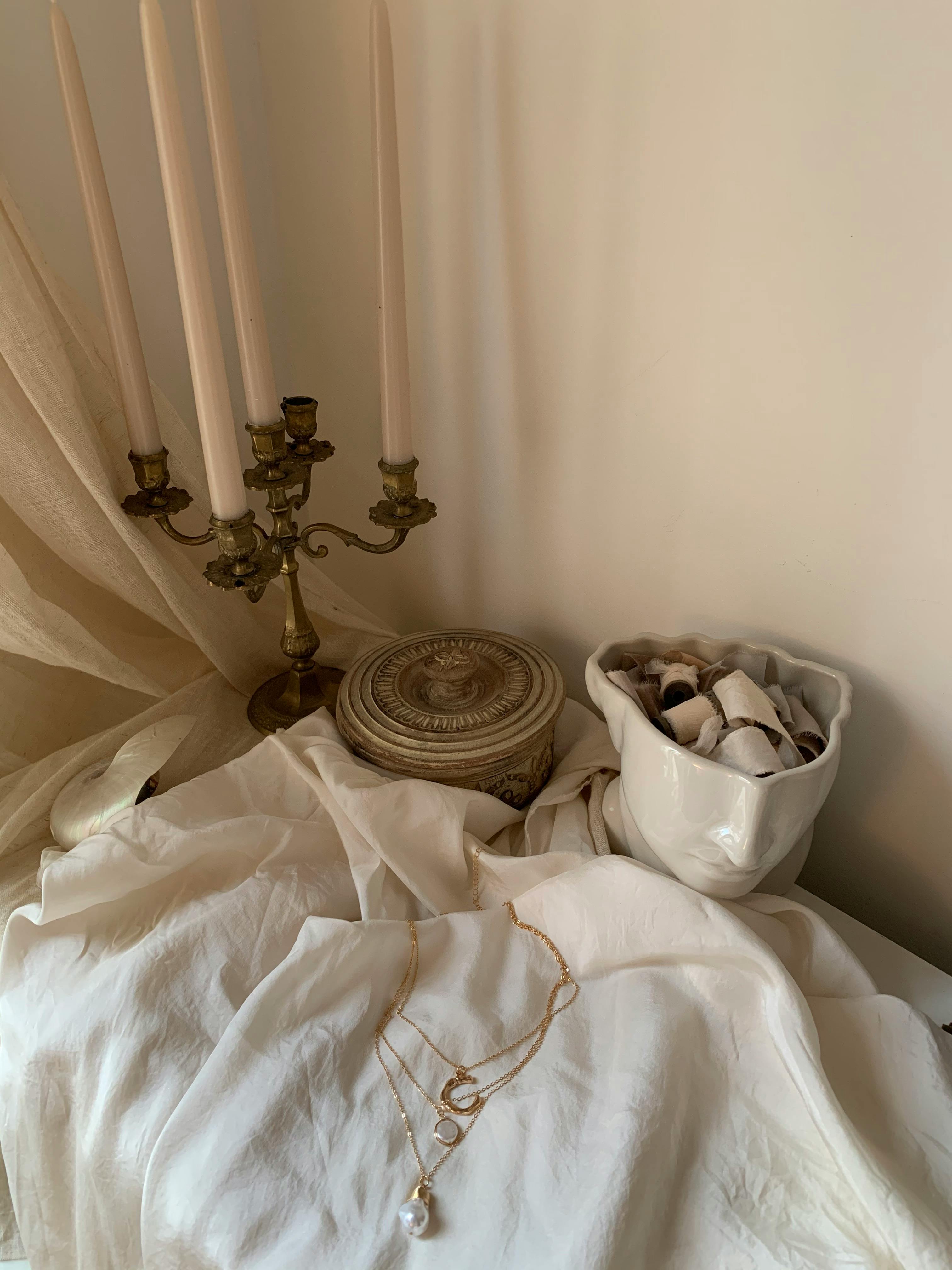 Charming still life featuring an antique candelabra, porcelain bust, and elegant jewelry on a draped fabric.