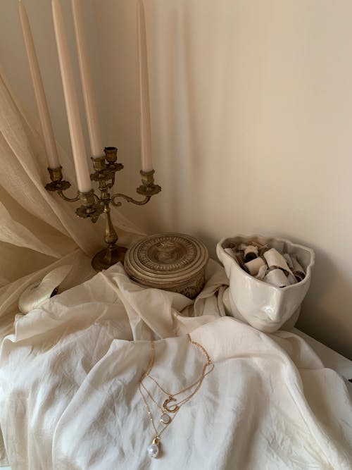 A white bed with a candle and a necklace