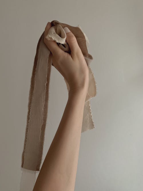 A hand holding a piece of fabric in front of a white wall