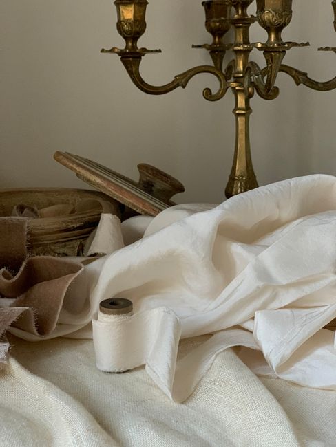 A classic still life featuring an antique brass candlestick, draped fabrics, and rustic elements.