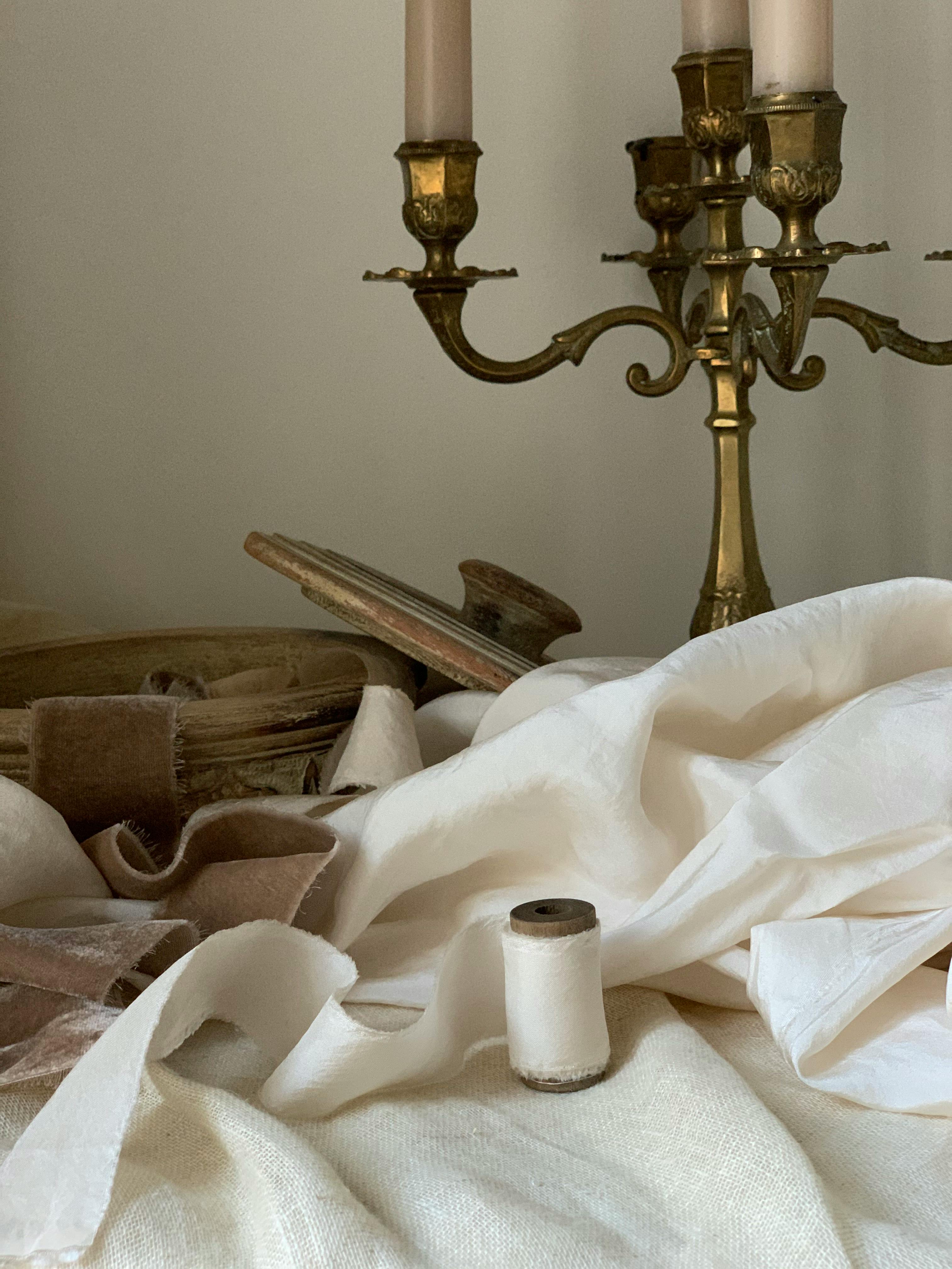 Artistic still life featuring a vintage brass candelabra, cloth, and ribbon.
