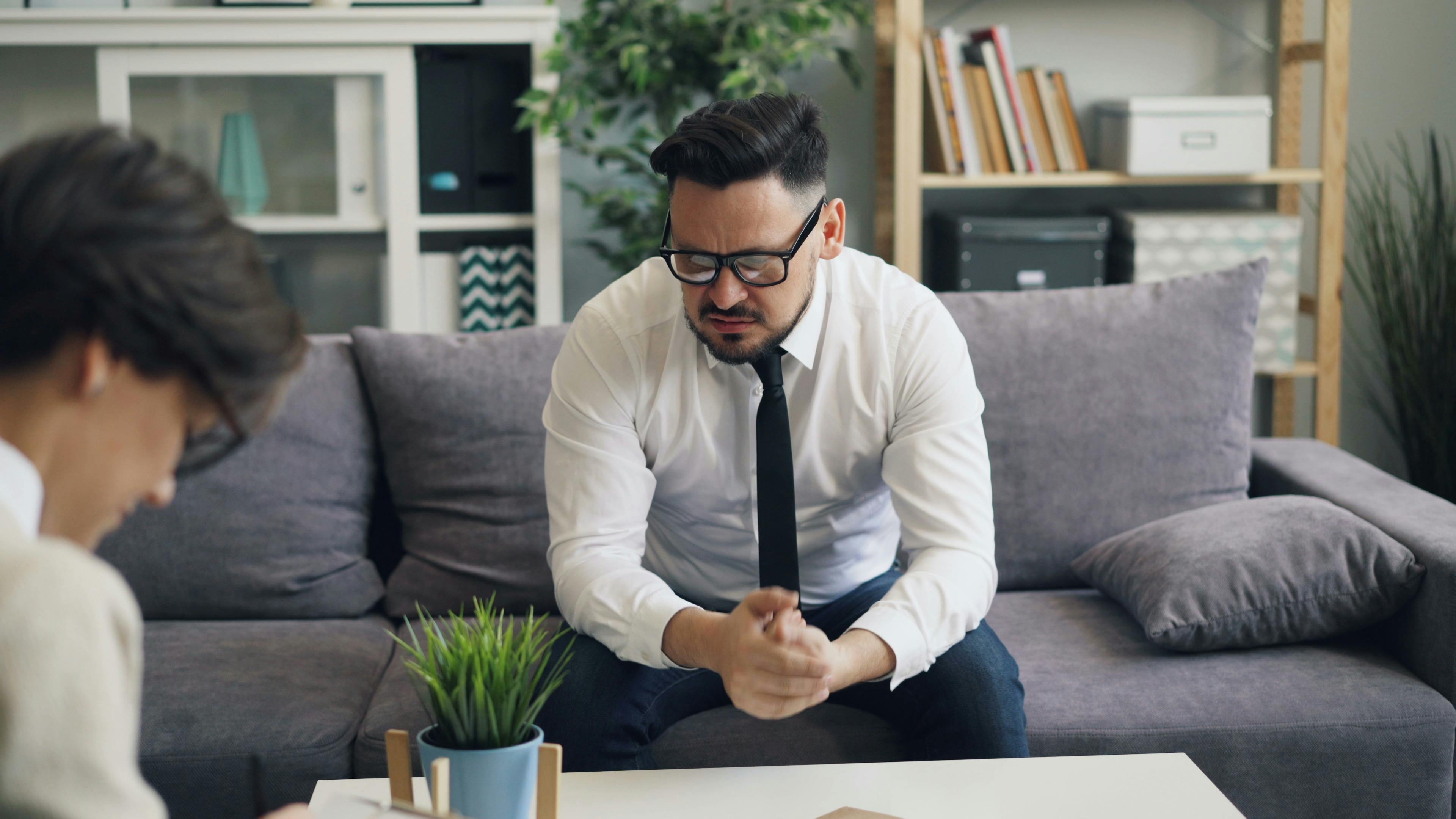 A stressed businessman in therapy session, showing visible emotions on a sofa.