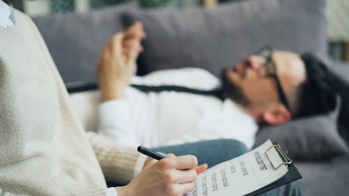 A man and woman are sitting on a couch with a clipboard