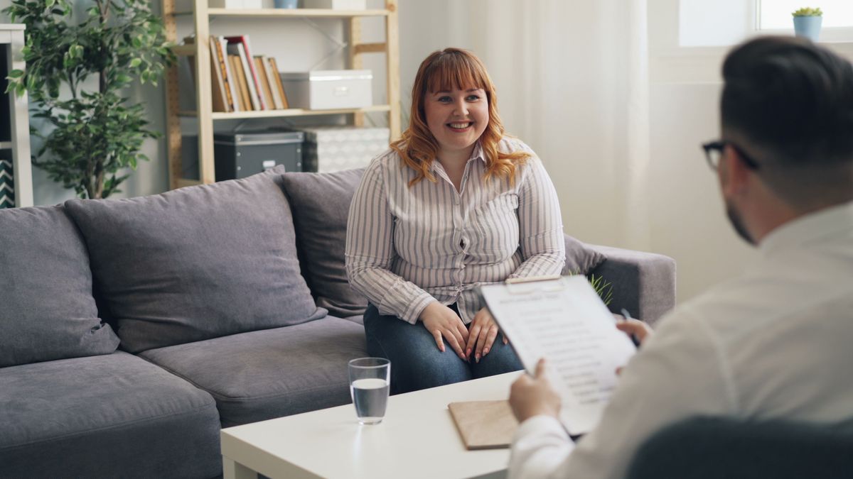 Two people talking across a low table with paperwork between them.