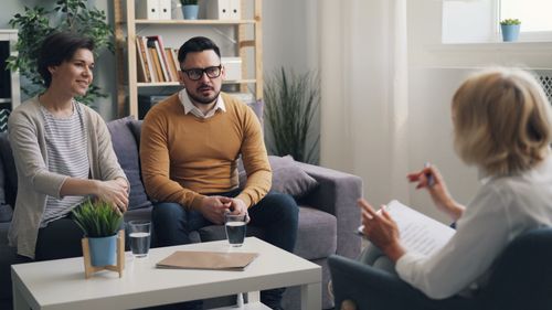 Free Couple discussing issues with therapist during a counseling session in a cozy office. Stock Photo