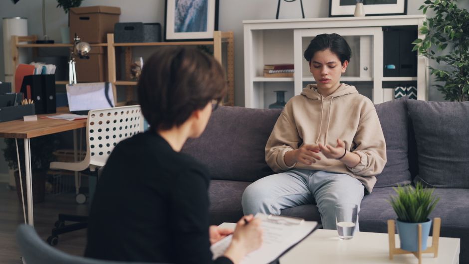 A teenager engages in a therapy session with a professional counselor in a modern office setting.
