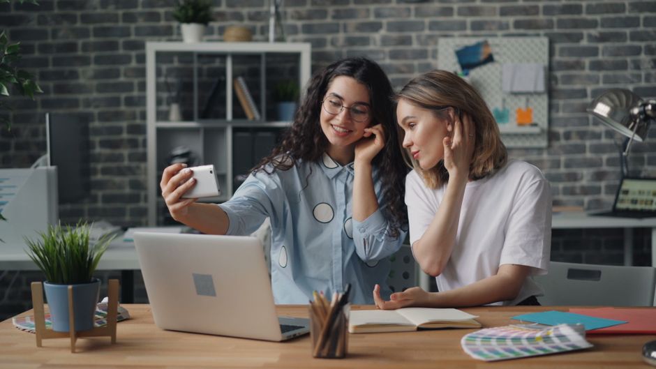 Two young women capture a selfie in a stylish office, enjoying a casual workday.