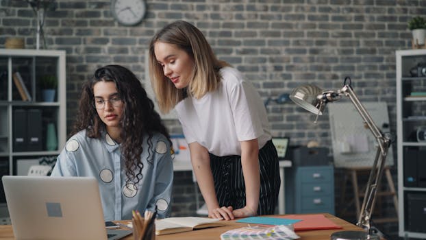 Two women working together on a laptop in a stylish, contemporary office setting.