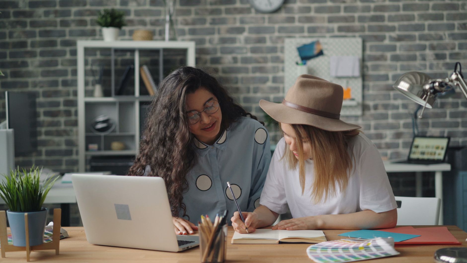 Two women working together in a modern office, discussing ideas over a laptop and notebook.