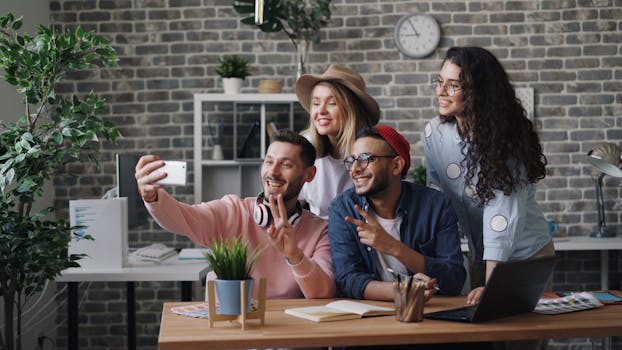 A group of young diverse coworkers smiling and taking a selfie in a stylish office setting.