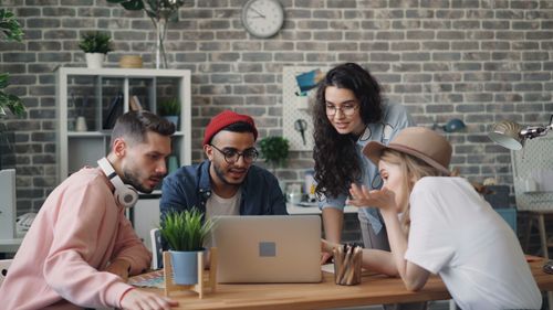 Free Young professionals collaborate in a modern office setting, focused on a laptop. Creative teamwork at its best. Stock Photo