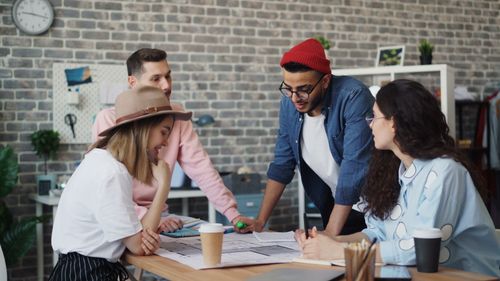 Free Young professionals collaborating on a project in a stylish office setting with casual teamwork atmosphere. Stock Photo