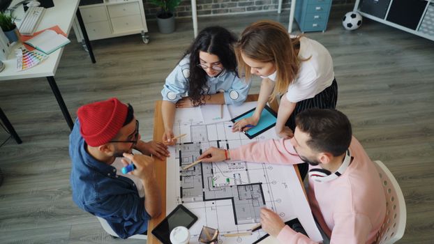 A diverse group of creative professionals collaborate on a floor plan in a modern office setting.