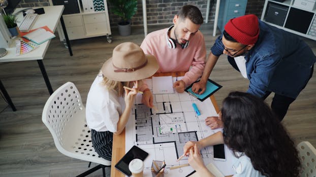 A diverse team works together on architectural plans around a table indoors.