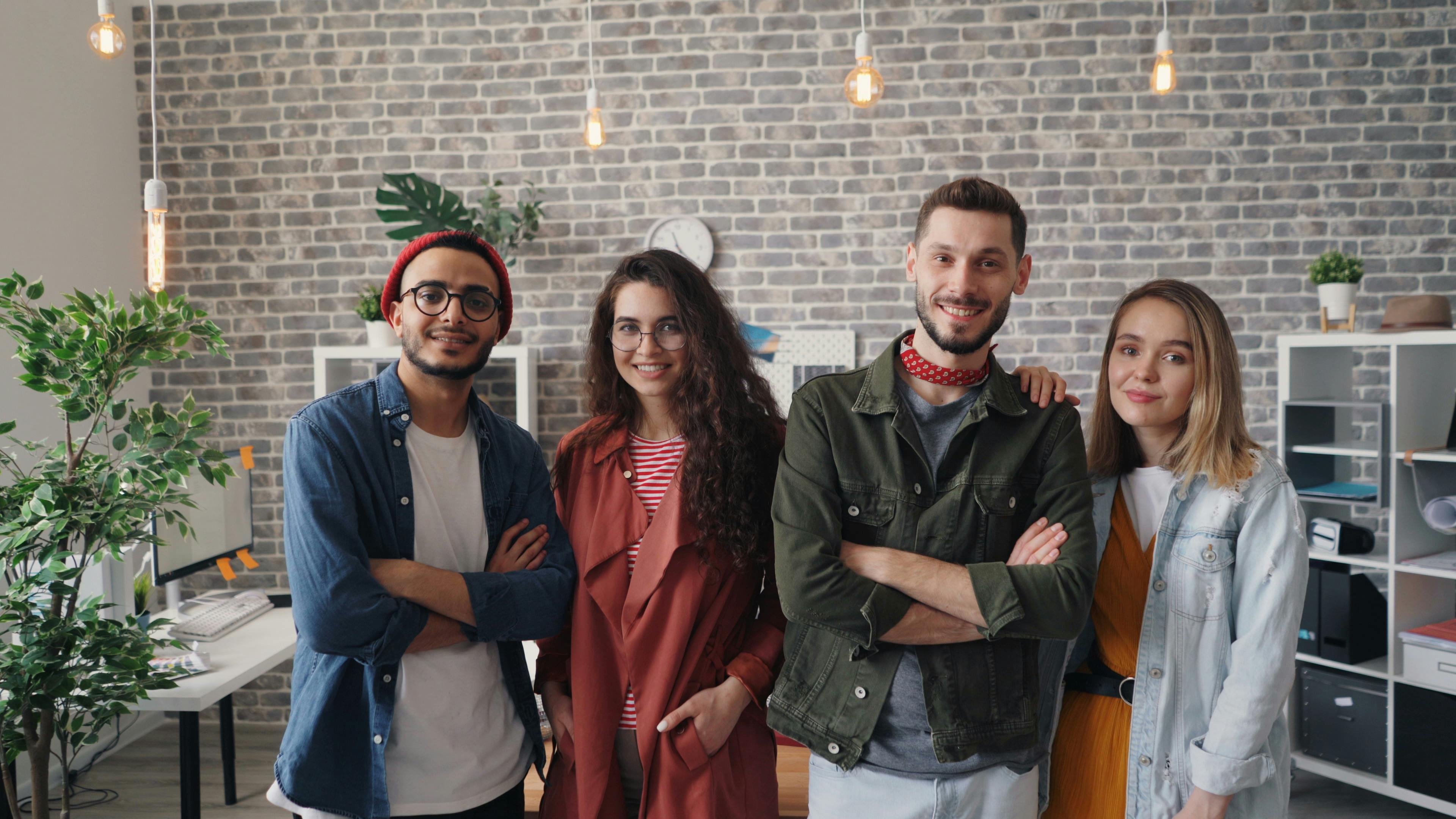Four young adults smiling in a modern office setting, showcasing teamwork and creativity.