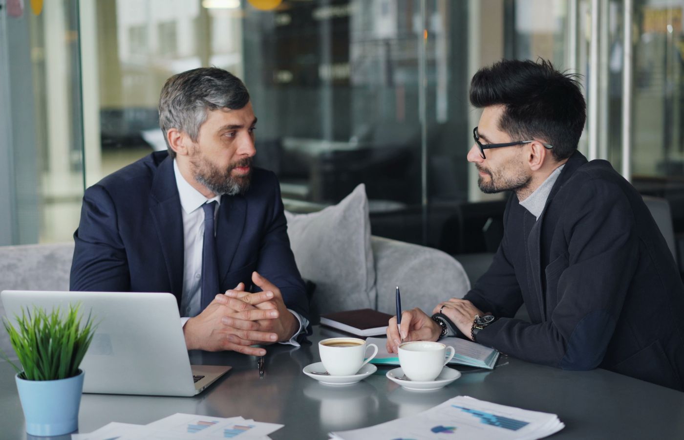 Two businessmen having a meeting with laptops, papers, and coffee at a modern office.