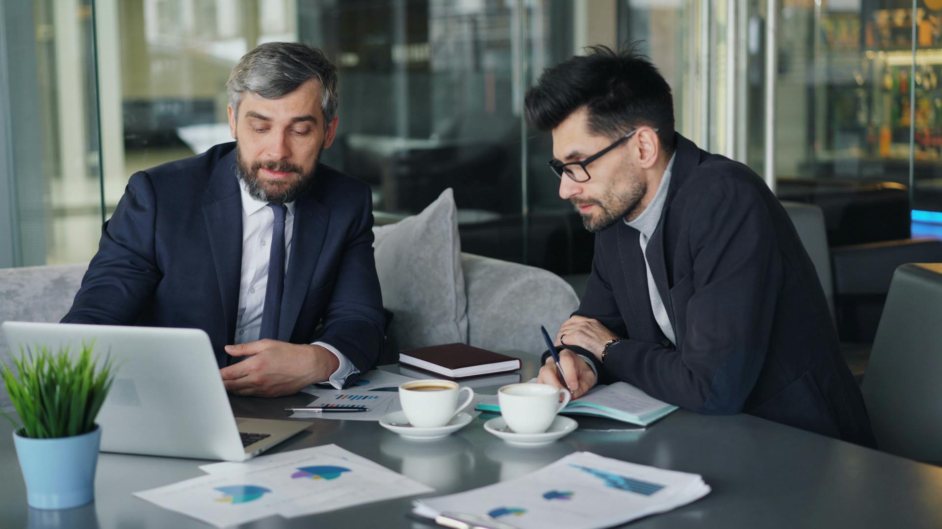 Businessmen Discussing Investments Over Laptop and Charts