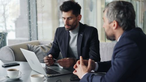Free Two businessmen engaged in a meeting in a cozy café, discussing on a laptop. Stock Photo