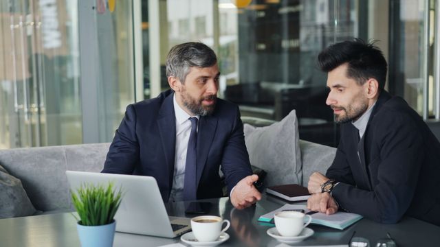 Deux professionnels échangent autour d’une table avec un carnet ouvert et un ordinateur portable.