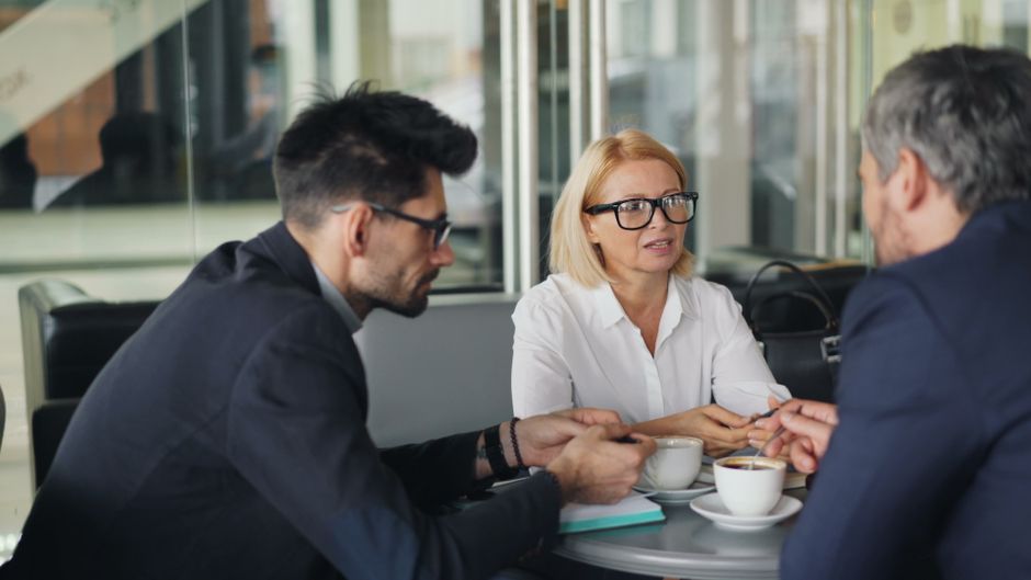 Equipo profesional discutiendo ideas mientras toma café en un ambiente moderno de cafetería.