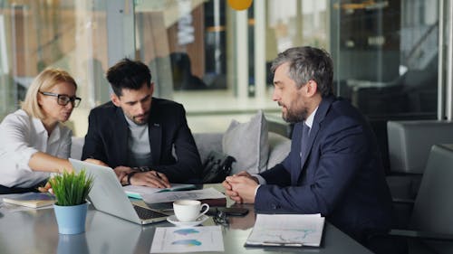 Three business people sitting around a table with laptops