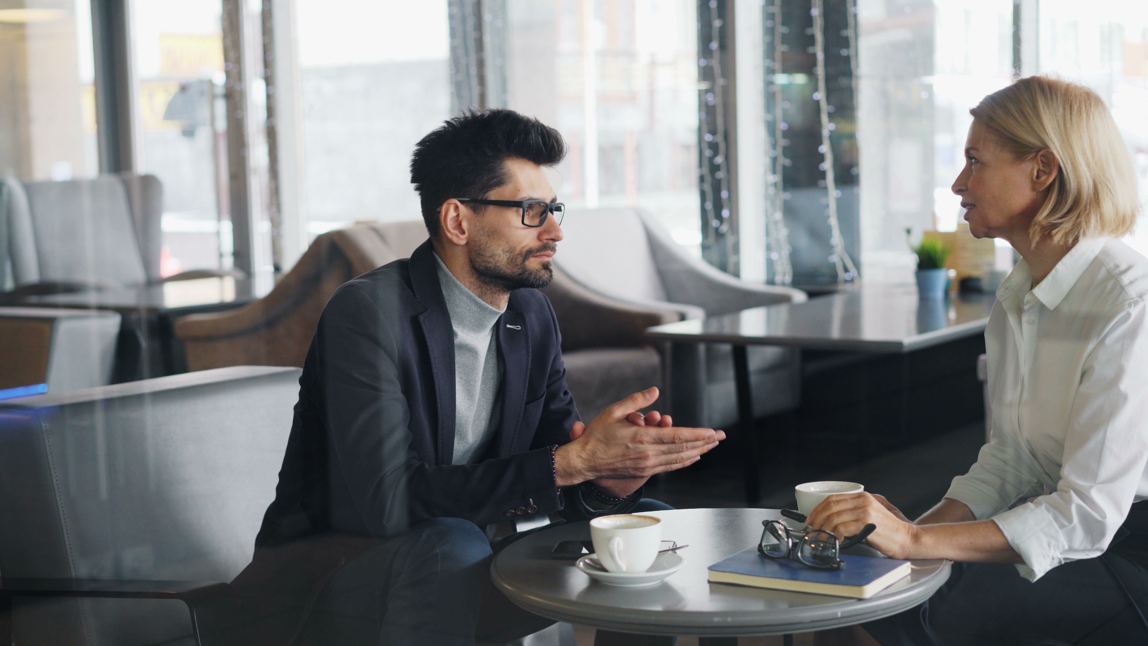 Professional man and woman discussing business topics over coffee in a contemporary cafe.
