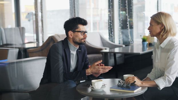 Professional man and woman discussing business topics over coffee in a contemporary cafe.