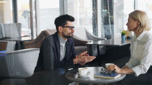 Free Professional man and woman discussing business topics over coffee in a contemporary cafe. Stock Photo