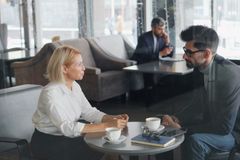 Two coworkers having a business meeting in a cozy café, discussing over coffee.