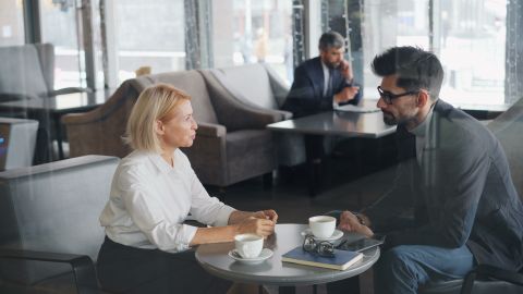 Two coworkers having a business meeting in a cozy café, discussing over coffee.