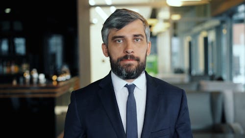 A man with a beard and a suit standing in a room