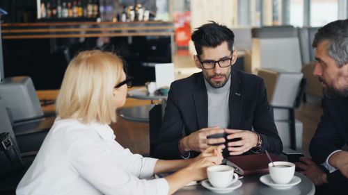 Free Three business professionals engaged in a strategic conversation at a café. Stock Photo