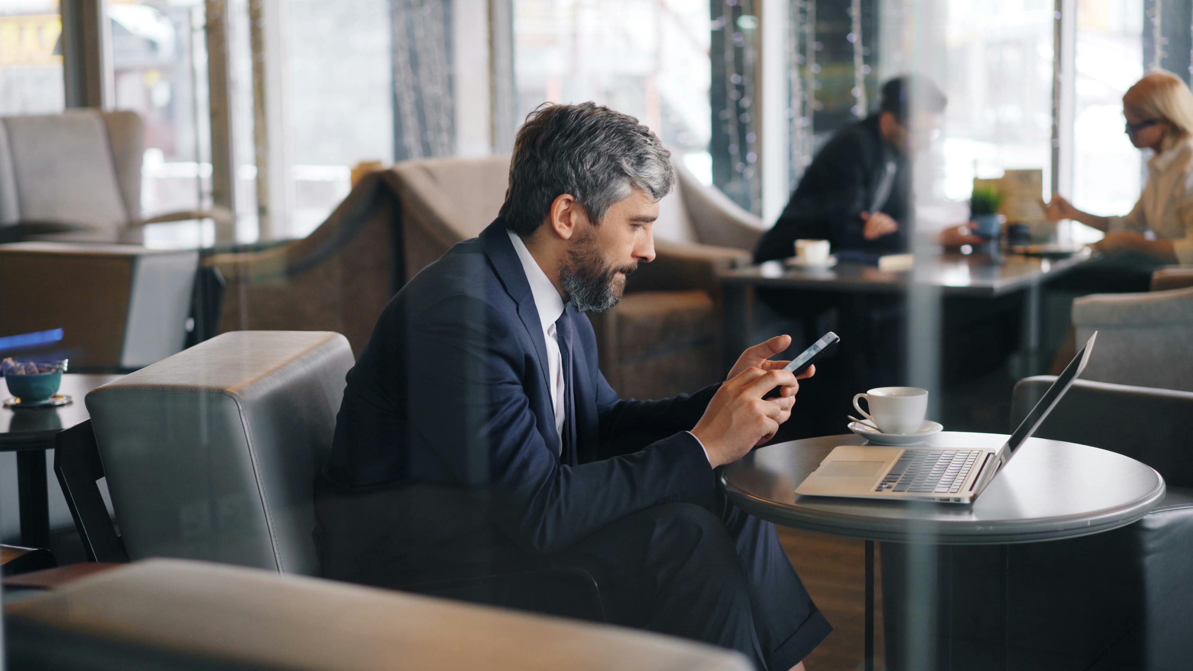 a man in a suit sitting at a table with a laptop and cell phone