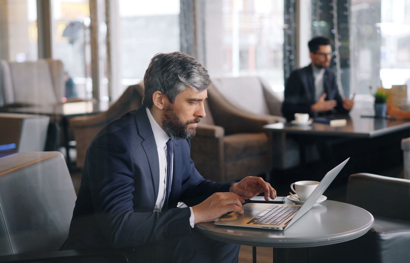 Businessman working on a laptop in a modern café setting, focused on tasks.