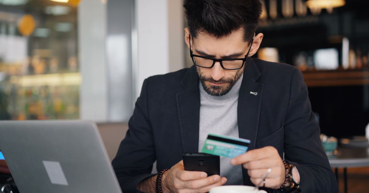 A man in glasses holding a payment card while looking at his phone.