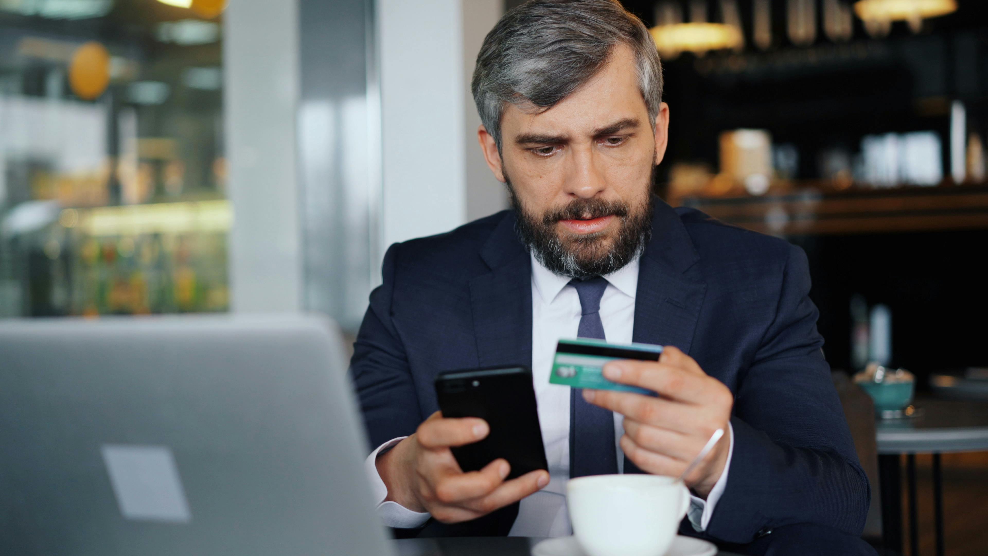 a man in a suit holding a credit card and a cell phone