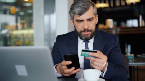 A man in a suit holding a credit card and a cell phone