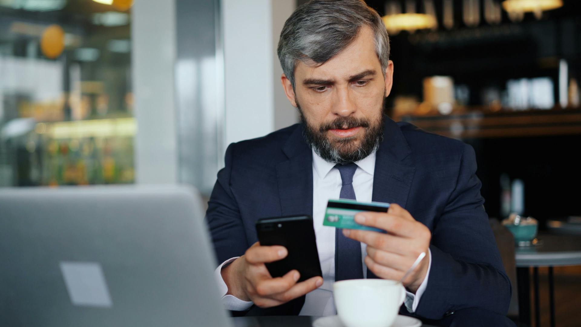 A man in a suit holding a credit card and a cell phone