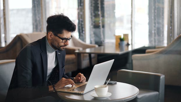 A stylish man in a cafe working on a laptop with coffee and modern decor.