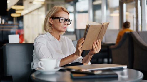 A woman in glasses reading a book at a table