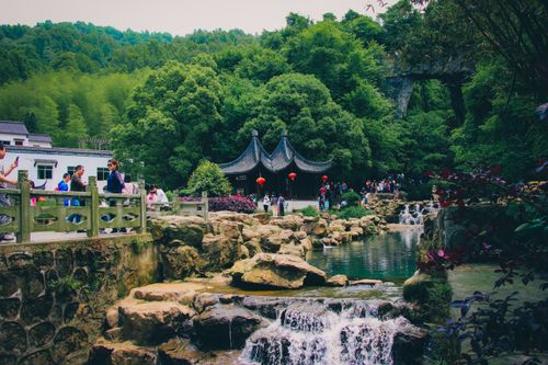 Free A serene traditional park with a stream, pavilion, and lush greenery, bustling with people. Stock Photo