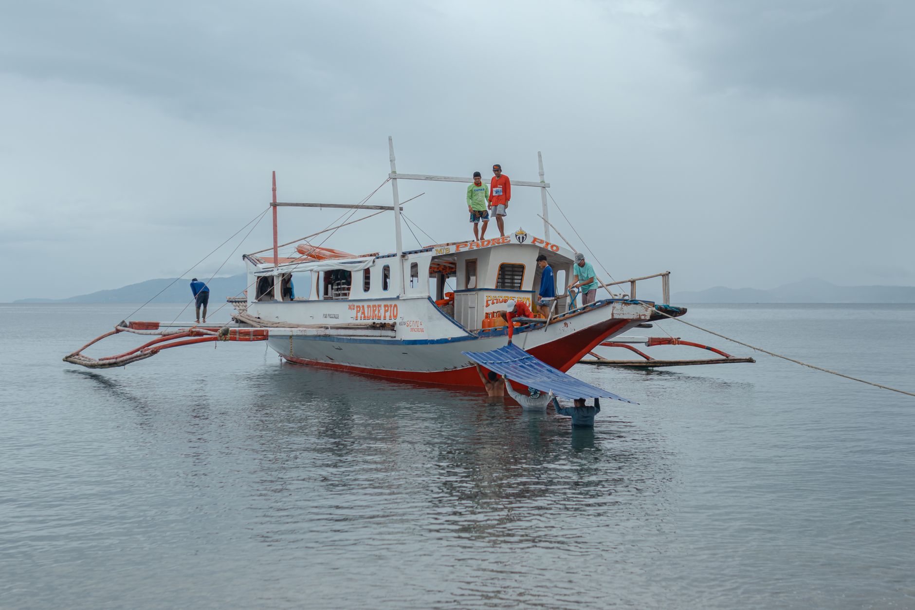 Traditional fishing boat on a serene lake, under an overcast sky with fishermen on board.